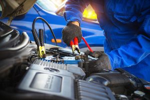 A person jump-starting a car engine using jumper cables on a battery under the hood. 