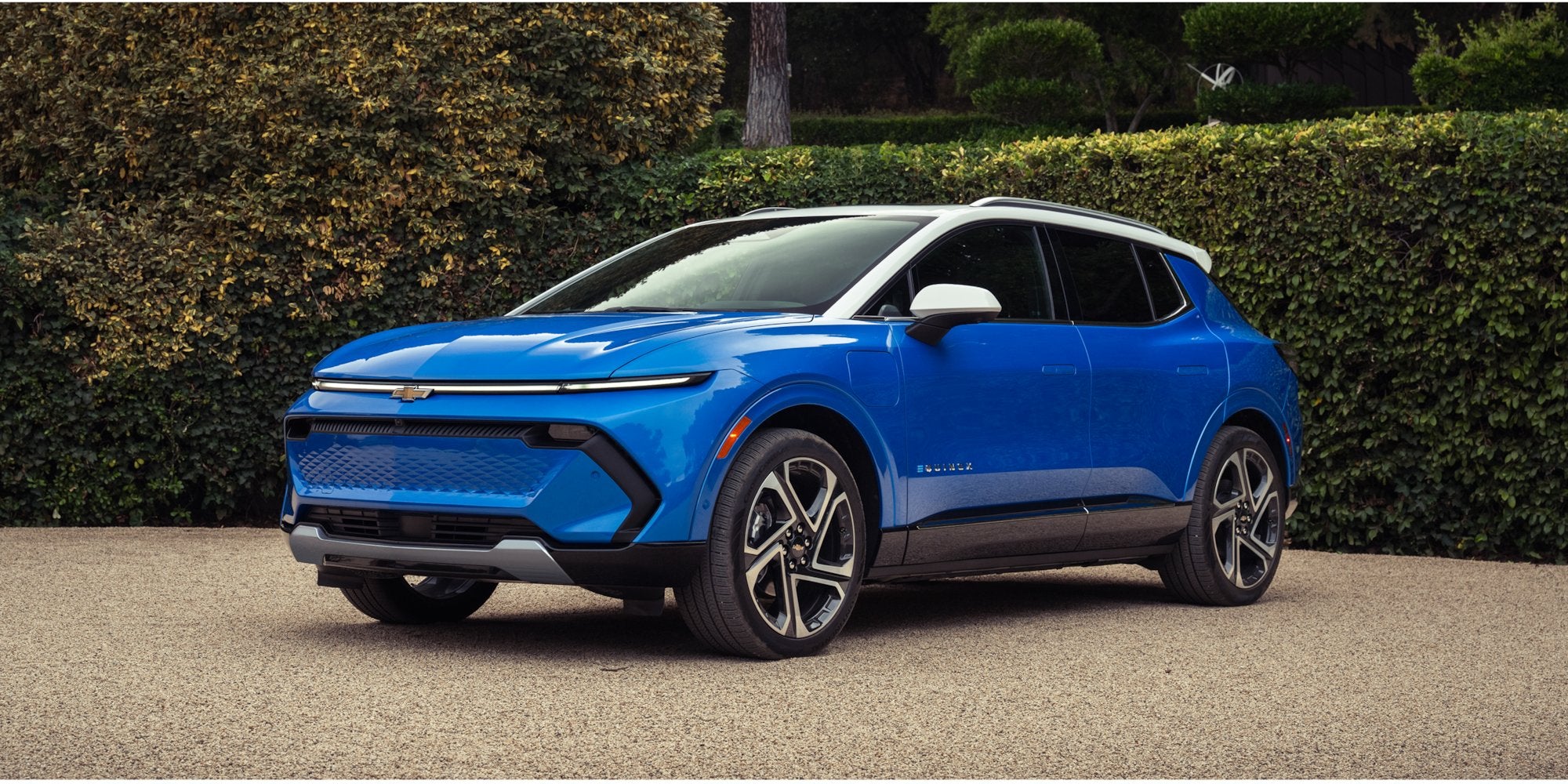 Blue Chevrolet Equinox EV parked in front of lush greenery.
